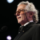 George Miller wears glasses and speaks into a microphone